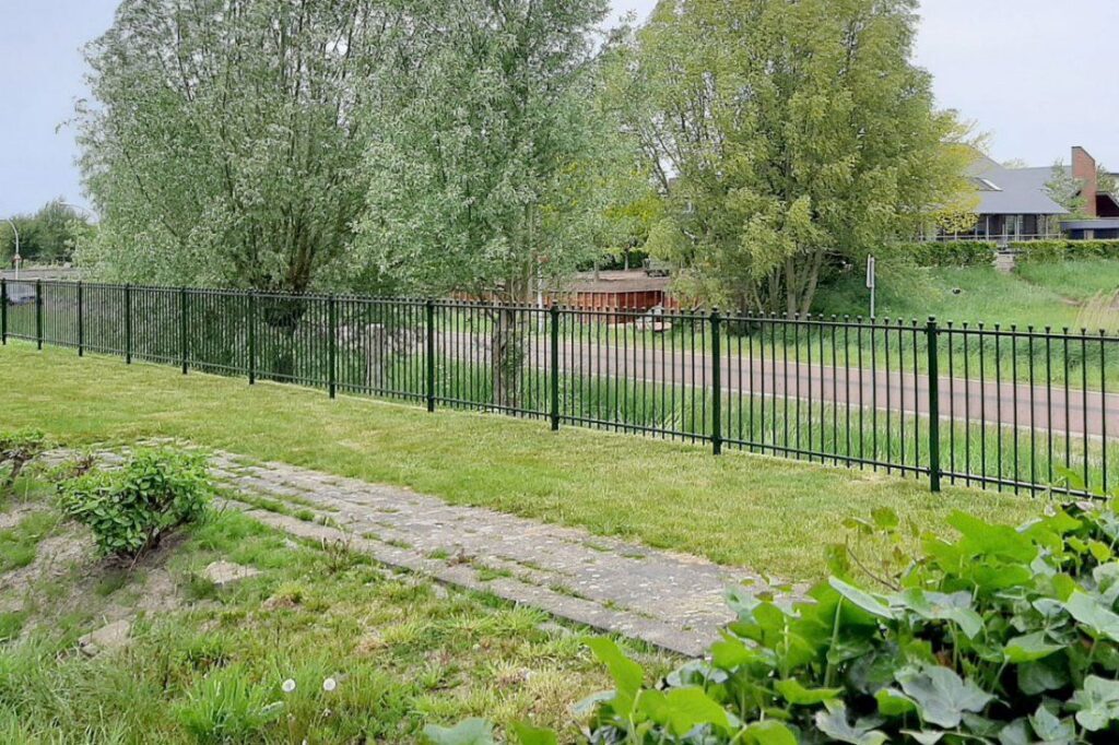 Zwart sierhekwerk langs een ruim erf met gazon en bomen