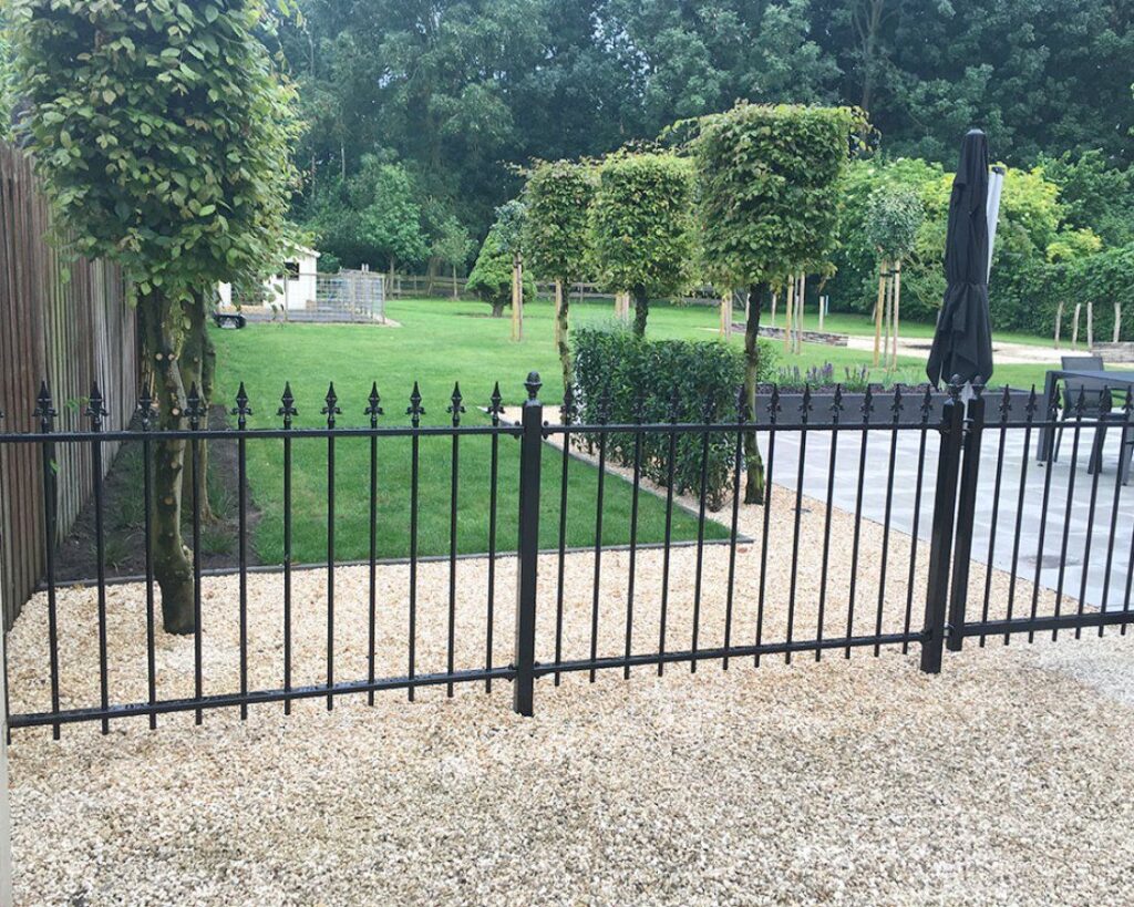 Sierhekwerk met speerpunten langs een grote tuin met leibomen