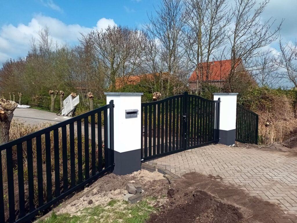 Donkergroene stalen spijlenpoort met naastgelegen hekwerk tussen witte pijlers