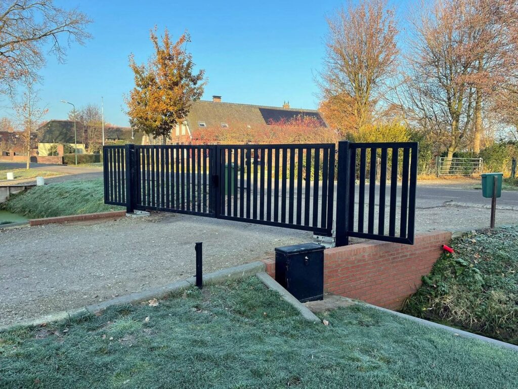 Antraciet stalen spijlenpoort aan stalen palen bij een oprit